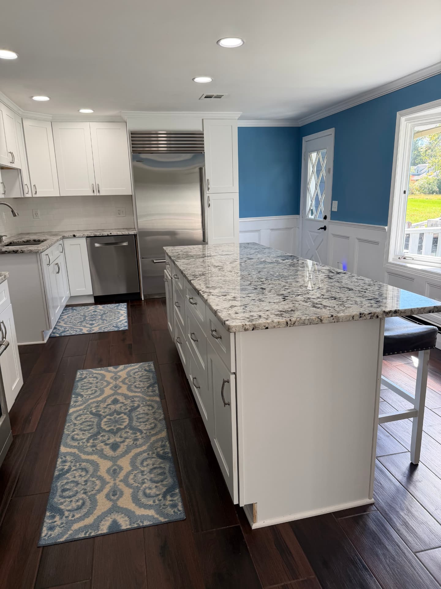 After kitchen renovation: granite-topped island with drawers beside blue walls and white wainscoting