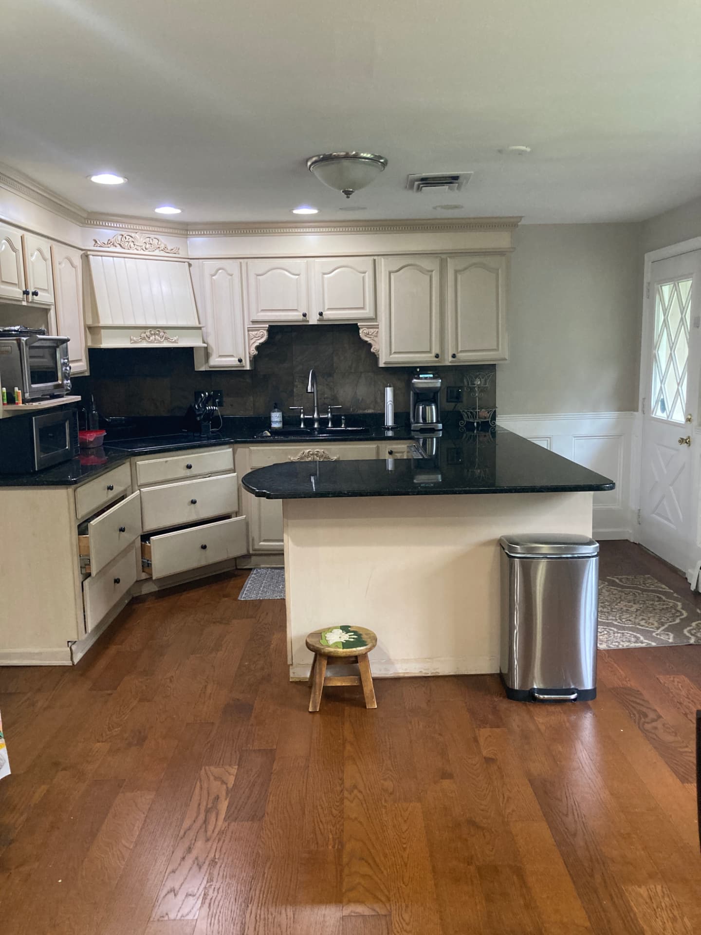 Before kitchen renovation: wider view of beige cabinetry, island and wood flooring