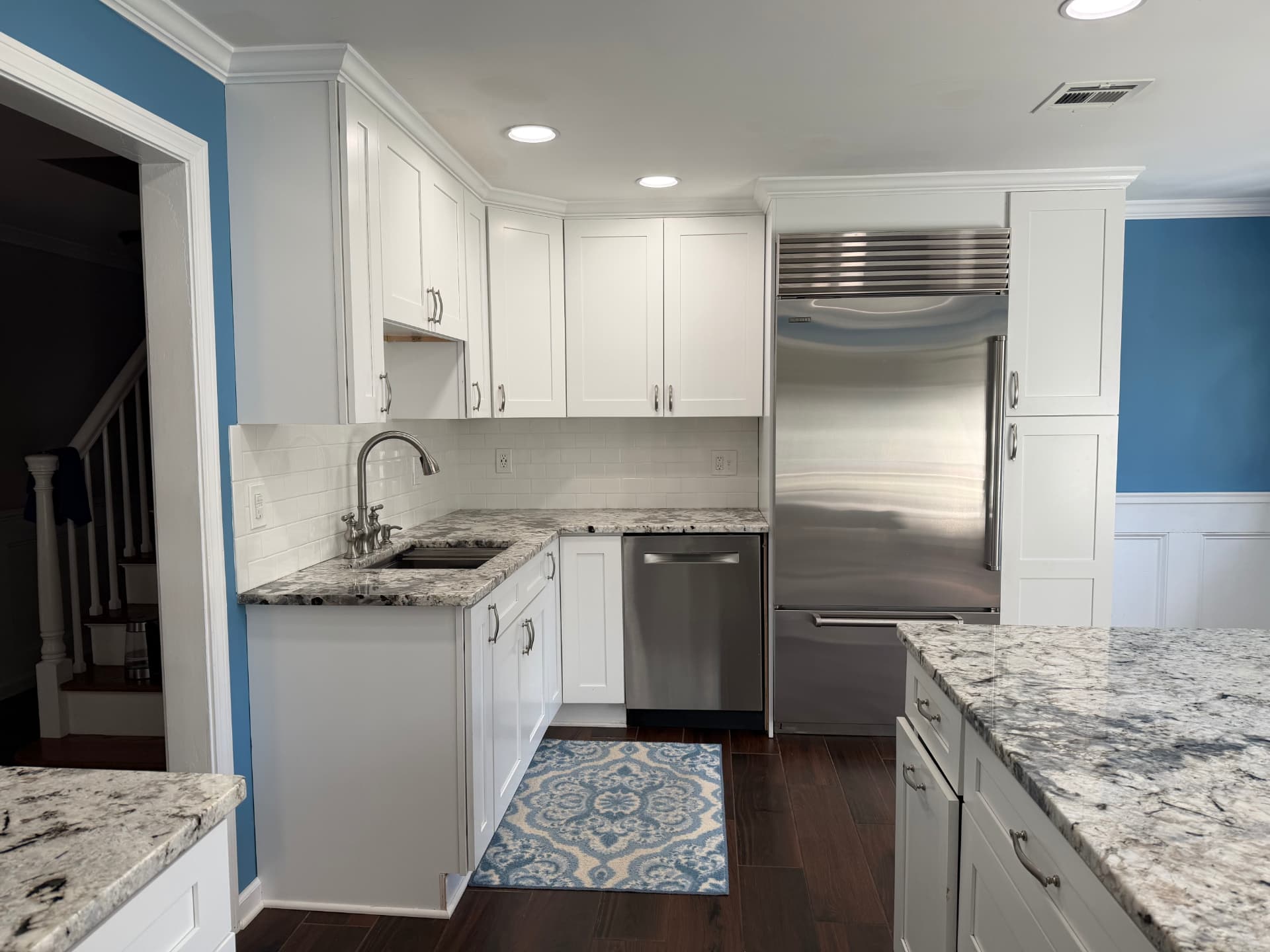 After kitchen renovation: corner sink, dishwasher and built-in stainless refrigerator framed by white cabinets