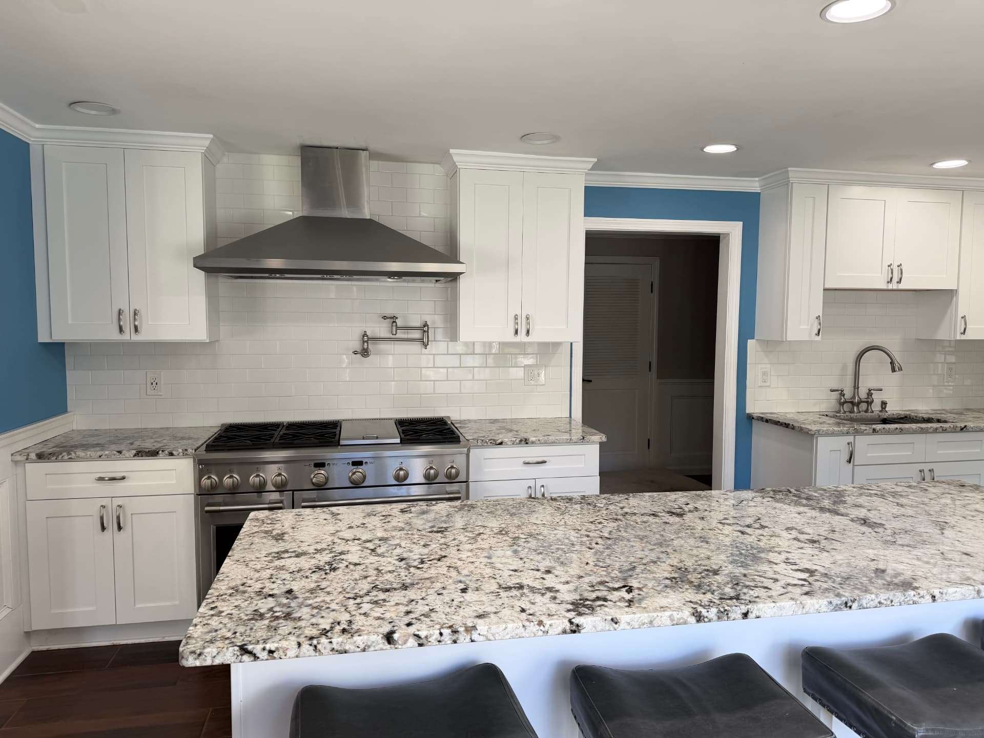 After kitchen renovation: white shaker cabinets, subway tile backsplash, stainless range hood and granite island