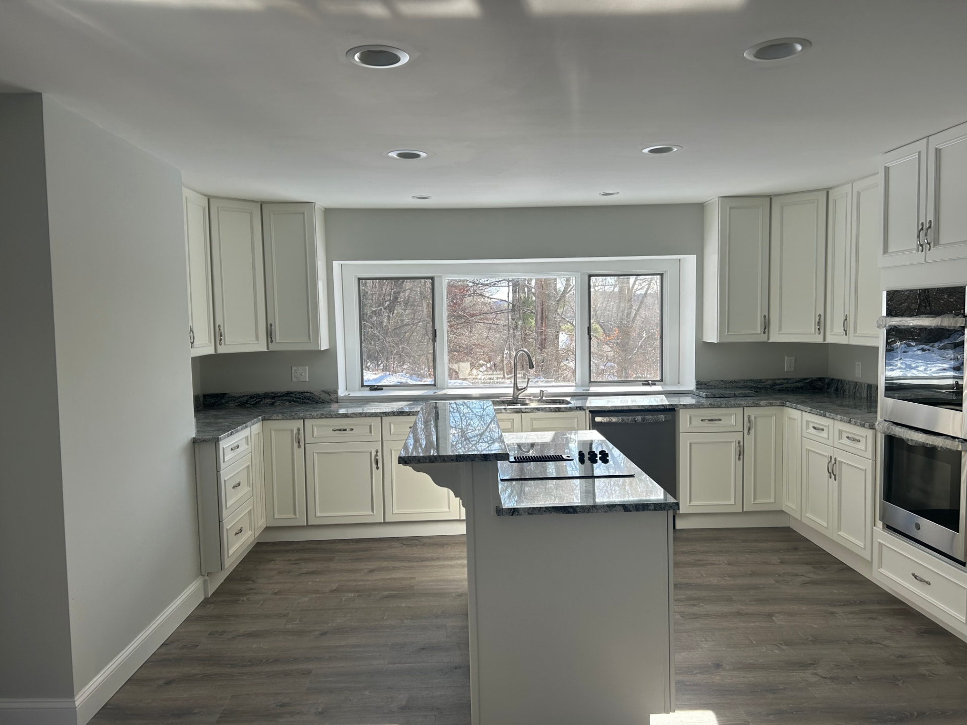 After kitchen rebuild: cream cabinets, granite countertops, double wall ovens and gray wood-look plank flooring